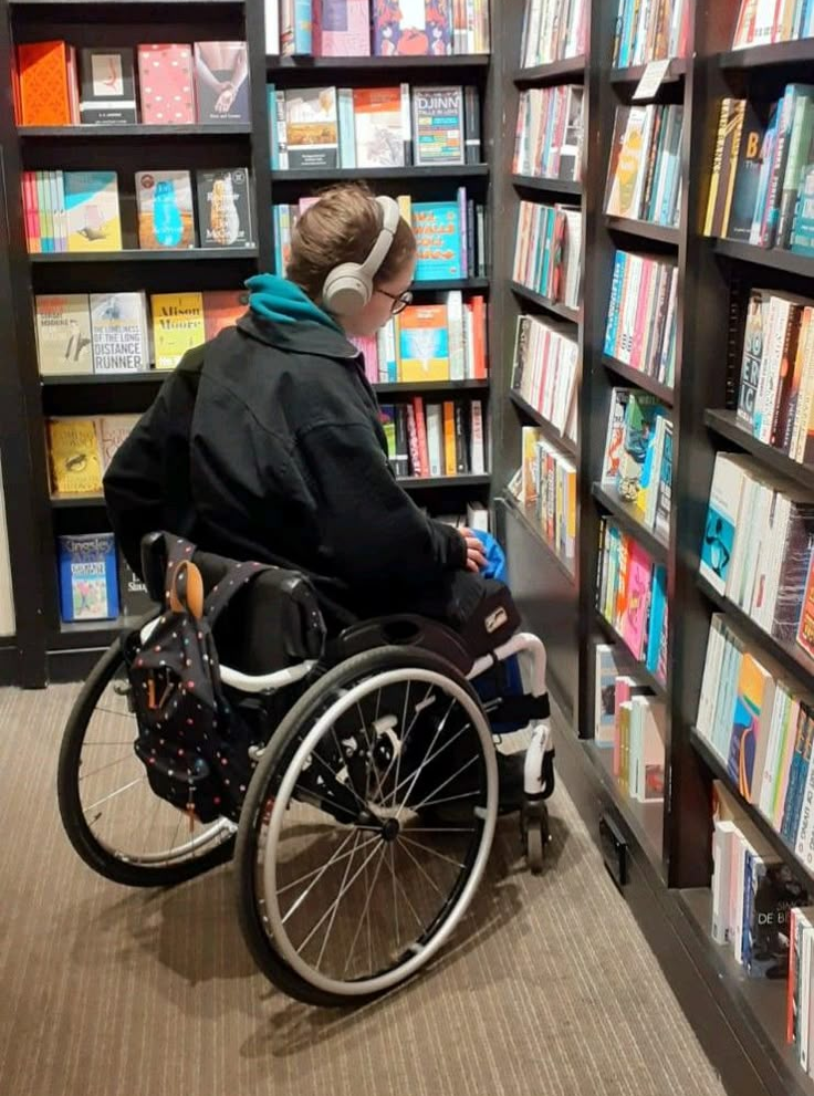 Person in wheelchair in a bookstore looking for books.